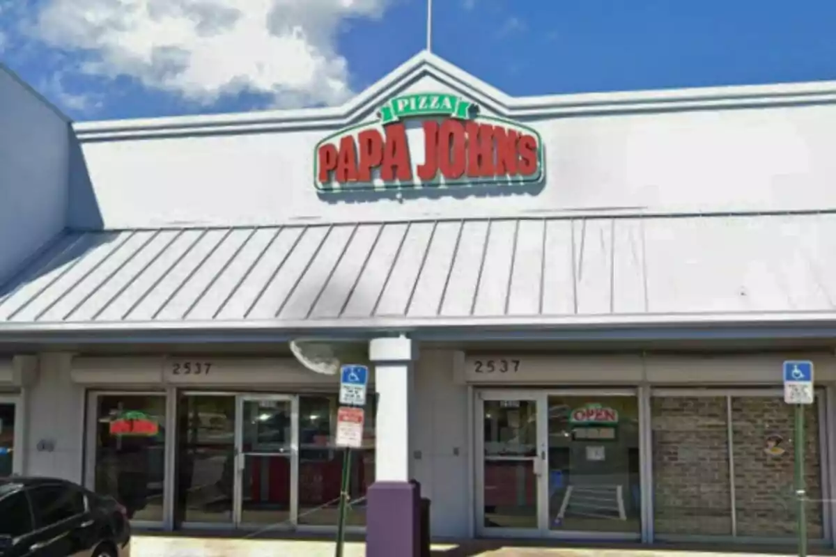Facade of a Papa John’s pizzeria with a visible sign and two accessible parking spaces in front Facade of a Papa John’s pizzeria with a visible sign and two accessible parking spaces in front