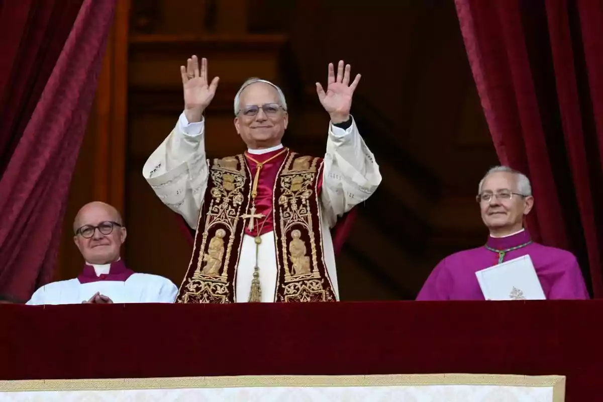 El Papa Lleó XIV vestit amb vestidures religioses aixeca les mans des d'un balcó acompanyat per dues persones més. El Papa Lleó XIV vestit amb vestidures religioses aixeca les mans des d'un balcó acompanyat per dues persones més.