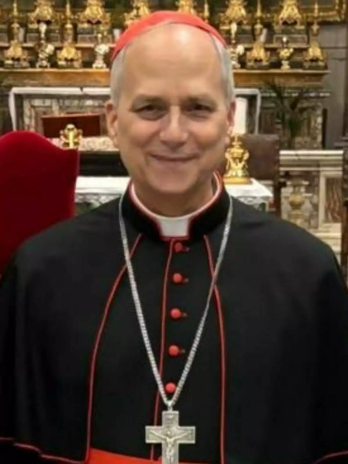 El Papa Lleó XIV vestit amb vestimenta eclesiàstica negra i vermella amb una creu penjant del seu coll somriu davant d'un altar decorat amb ornaments daurats. El Papa Lleó XIV vestit amb vestimenta eclesiàstica negra i vermella amb una creu penjant del seu coll somriu davant d'un altar decorat amb ornaments daurats.