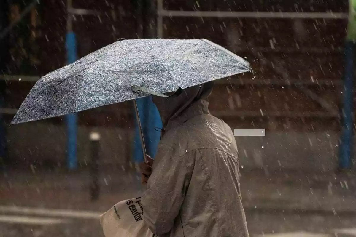 Dona amb un paraigua al carrer al mig d'un temporal de pluja