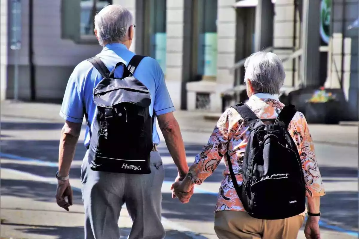 Un home i una dona grans caminant pel carrer amb motxilles