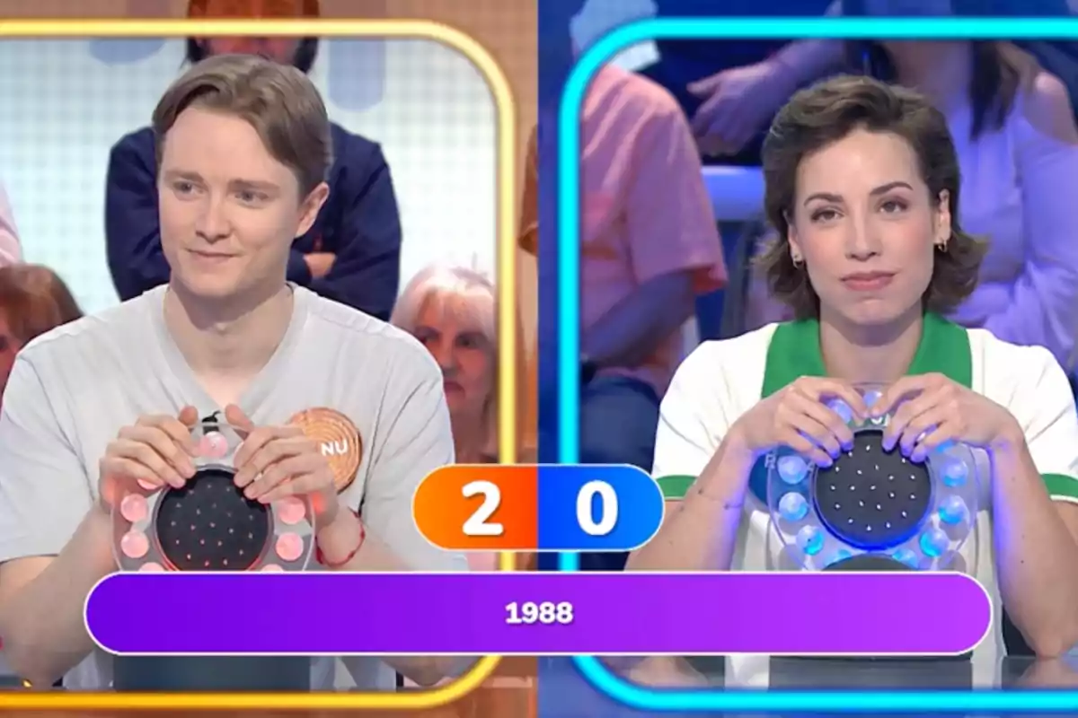 Manu i Rosa participen en un programa de televisió de preguntes i respostes, cadascun sosté un polsador i el marcador mostra 2 a 0 amb l'any 1988 a la pantalla. Captura de 'Pasapalabra' Manu i Rosa participen en un programa de televisió de preguntes i respostes, cadascun sosté un polsador i el marcador mostra 2 a 0 amb l'any 1988 a la pantalla. Captura de 'Pasapalabra'