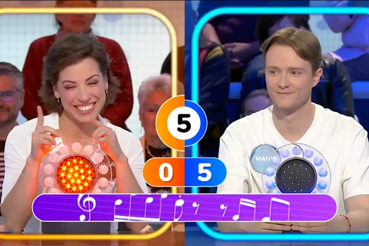 La Rosa i en Manu somriuen en un programa de jocs de televisió, cadascun amb un panell de llums davant seu, mentre el marcador central mostra una puntuació de cinc a zero i una partitura musical apareix a la part inferior de la imatge. Captura de 'Pasapalabra'