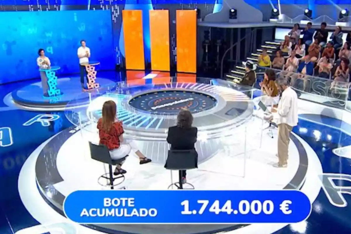 Un plató de concurs televisiu amb concursants, presentador, públic i un marcador que mostra un pot acumulat de 1.744.000 euros. Captura de 'Pasapalabra' Un plató de concurs televisiu amb concursants, presentador, públic i un marcador que mostra un pot acumulat de 1.744.000 euros. Captura de 'Pasapalabra'