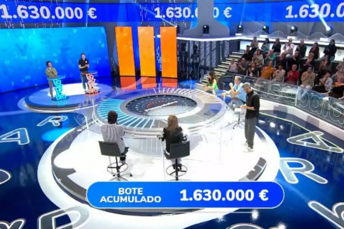 Un plató de concurs televisiu amb participants i públic, mostrant un pot acumulat de 1.630.000 euros en una pantalla. Captura de 'Pasapalabra'. Un plató de concurs televisiu amb participants i públic, mostrant un pot acumulat de 1.630.000 euros en una pantalla. Captura de 'Pasapalabra'.