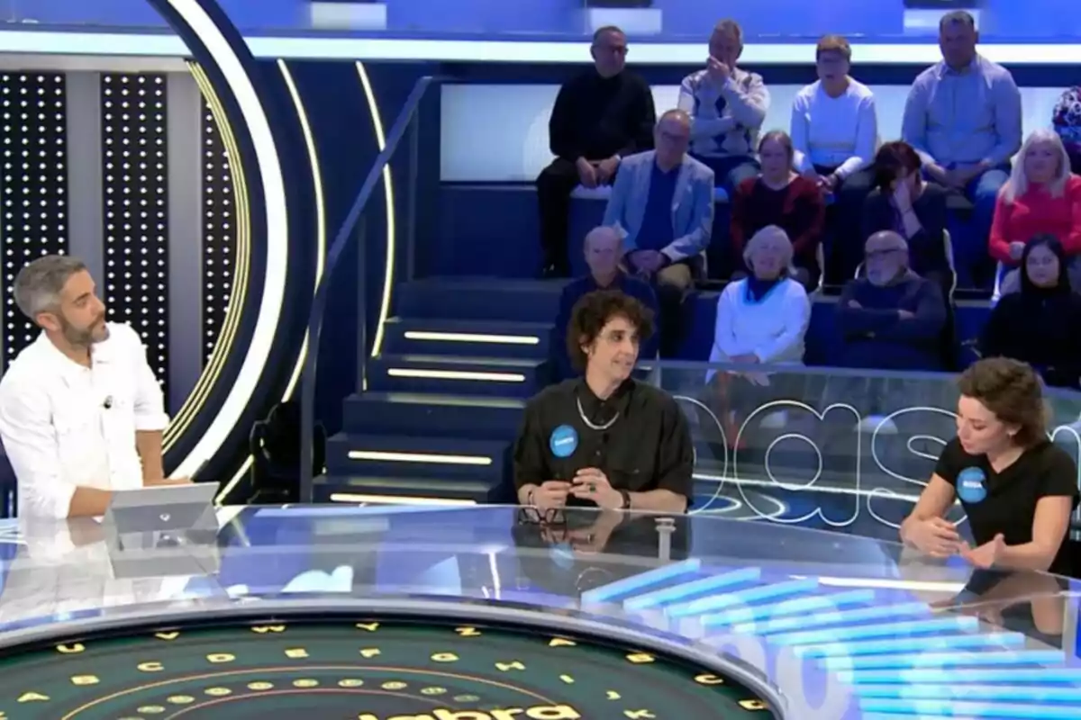 Roberto Leal interactua amb Canco Rodríguez i Rosa en un plató de programa de jocs, mentre el públic observa des de les grades. Captura de 'Pasapalabra'. Roberto Leal interactua amb Canco Rodríguez i Rosa en un plató de programa de jocs, mentre el públic observa des de les grades. Captura de 'Pasapalabra'.
