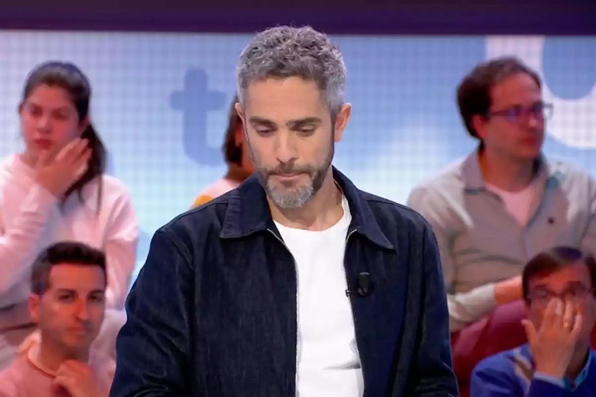 Roberto Leal, vestit amb jaqueta fosca i samarreta blanca, és en un estudi de televisió amb persones assegudes al fons. Captura de 'Pasapalabra'. Roberto Leal, vestit amb jaqueta fosca i samarreta blanca, és en un estudi de televisió amb persones assegudes al fons. Captura de 'Pasapalabra'.