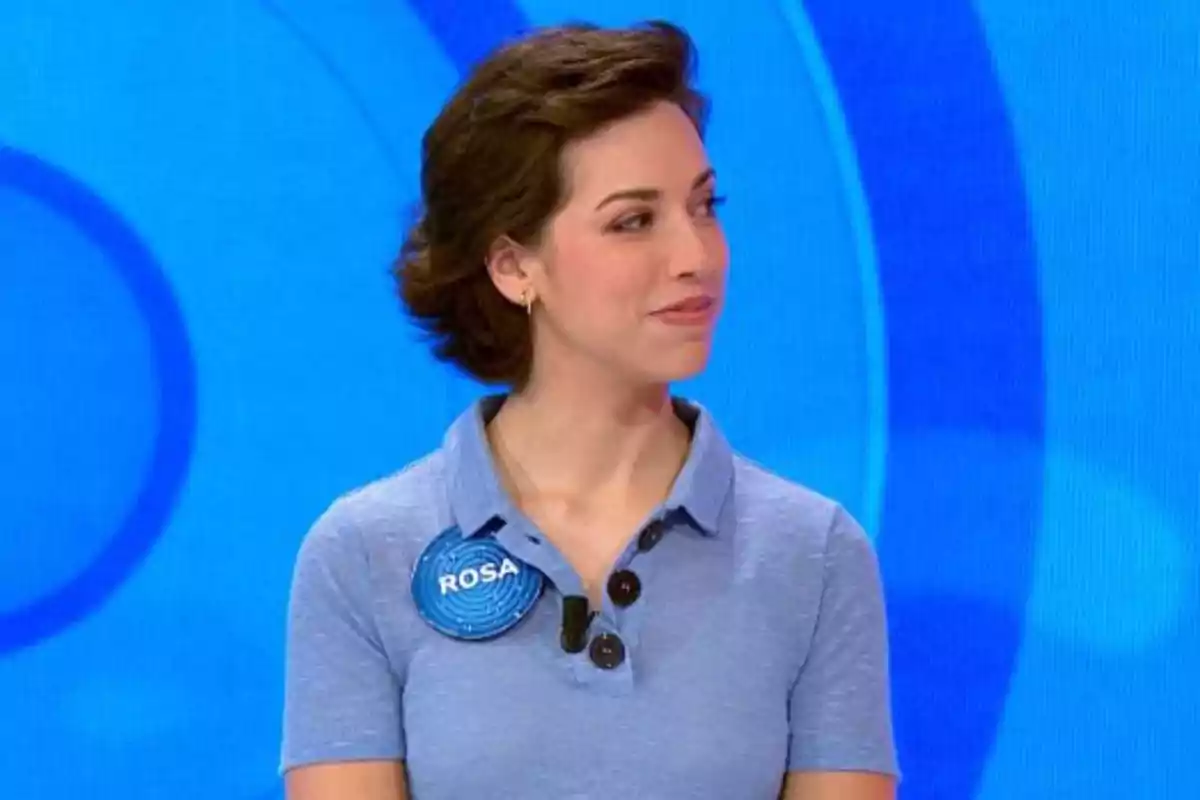 Rosa porta una camisa blau clar i una xapa amb el nom Rosa, és en un plató de televisió amb fons blau. Captura de 'Pasapalabra' Rosa porta una camisa blau clar i una xapa amb el nom Rosa, és en un plató de televisió amb fons blau. Captura de 'Pasapalabra'