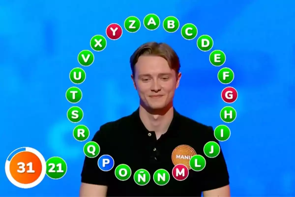 Manu en un programa de televisió està dret davant d'una pantalla blava amb lletres de l'alfabet en cercles de colors al seu voltant i un marcador de temps a la cantonada inferior esquerra. Captura de 'Pasapalabra'. Manu en un programa de televisió està dret davant d'una pantalla blava amb lletres de l'alfabet en cercles de colors al seu voltant i un marcador de temps a la cantonada inferior esquerra. Captura de 'Pasapalabra'.