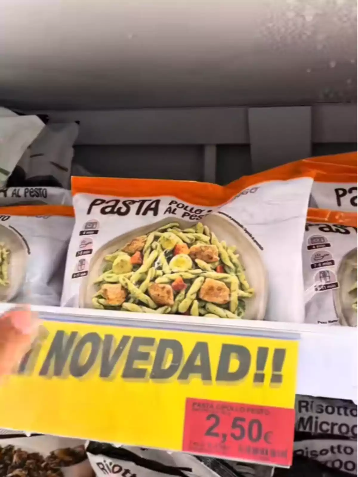 Paquet de pasta amb pollastre al pesto en un prestatge de supermercat amb un cartell groc que diu Paquet de pasta amb pollastre al pesto en un prestatge de supermercat amb un cartell groc que diu