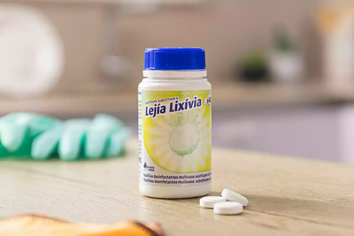 Un pot de pastilles desinfectants multiusos amb tapa blava sobre una taula de fusta en una cuina, al costat de tres pastilles soltes. Un pot de pastilles desinfectants multiusos amb tapa blava sobre una taula de fusta en una cuina, al costat de tres pastilles soltes.