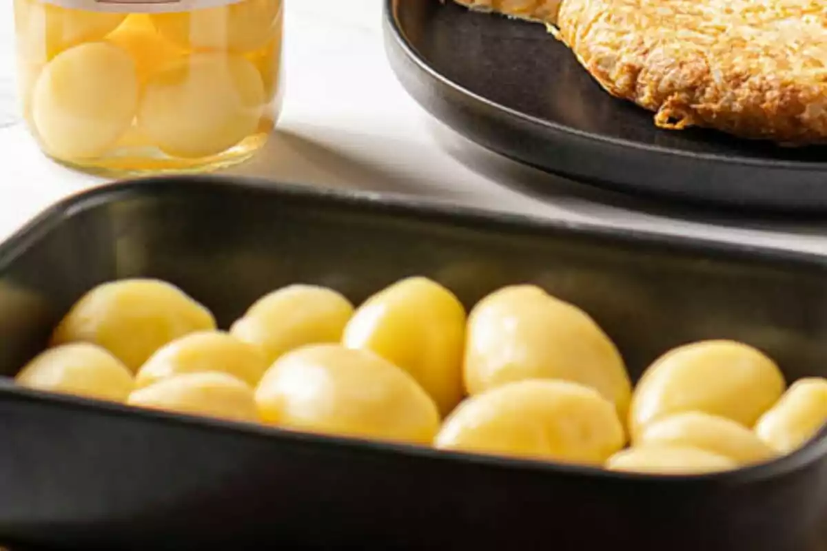 Un plat de patates bullides al costat d'un pot de patates en conserva i una truita en un plat negre. Un plat de patates bullides al costat d'un pot de patates en conserva i una truita en un plat negre.