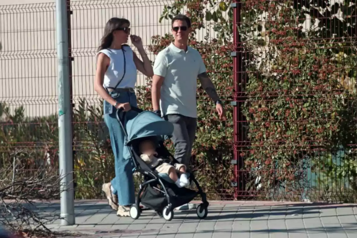 Patricia Pardo i Christian Gálvez passeja amb un cotxet de nadó per una vorera, envoltats de vegetació i una tanca de metall. Patricia Pardo i Christian Gálvez passeja amb un cotxet de nadó per una vorera, envoltats de vegetació i una tanca de metall.