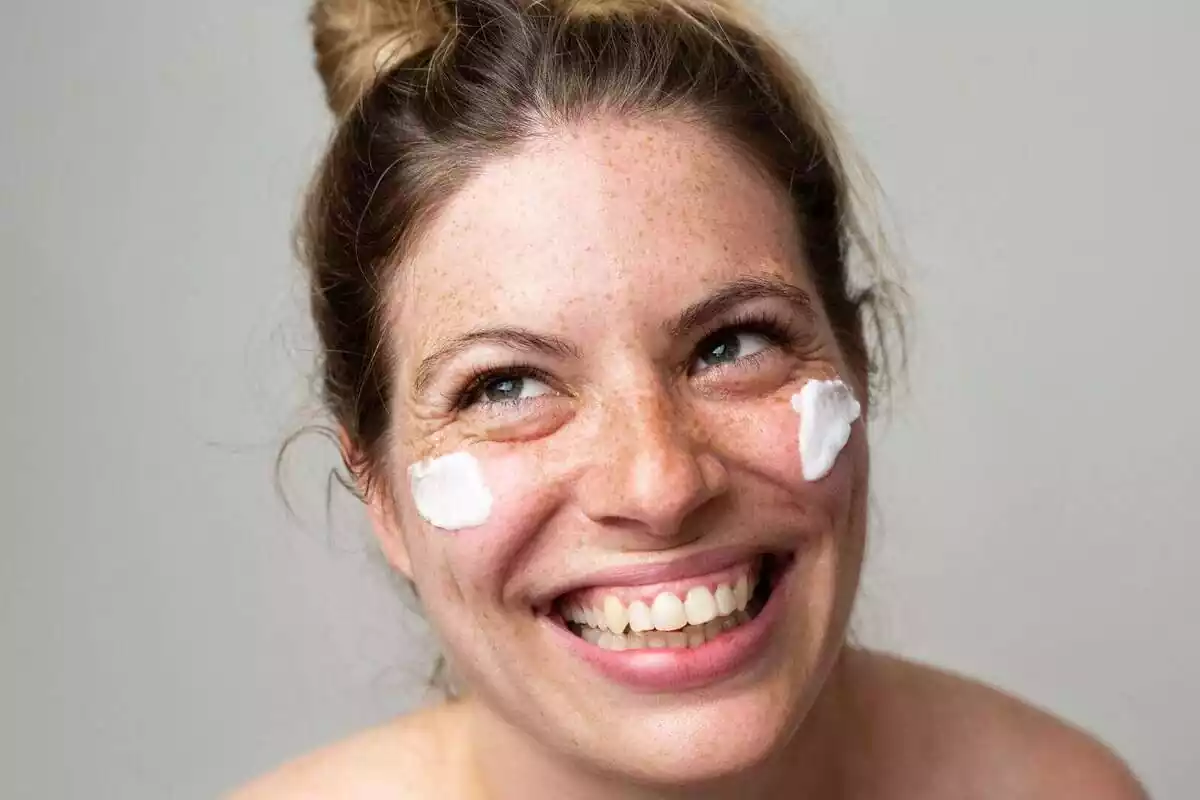 Dona somrient amb pigues i crema solar a la cara