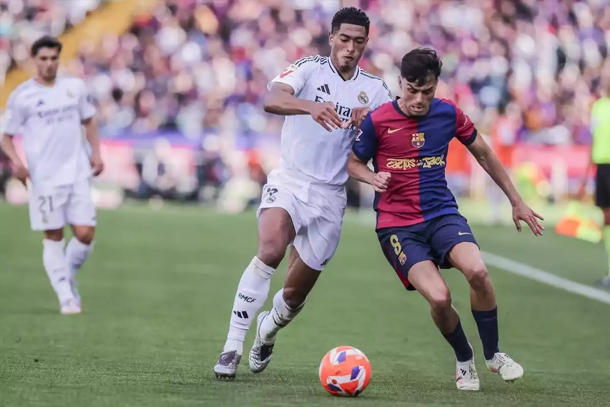 Dos jugadors de futbol competeixen per la pilota en un partit, un vesteix de blanc i l'altre de blau i vermell. Dos jugadors de futbol competeixen per la pilota en un partit, un vesteix de blanc i l'altre de blau i vermell.