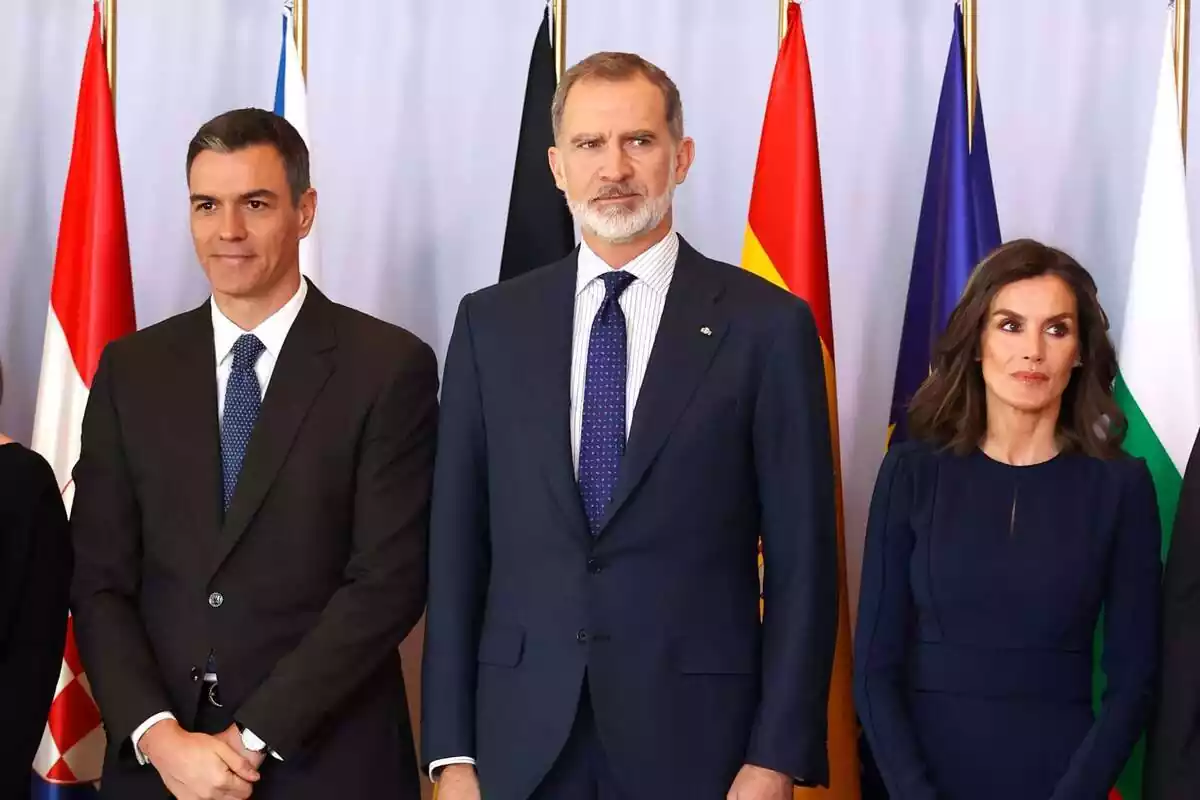 Pedro Sánchez smiling with his hands together next to a serious Felipe VI with a blue tie and Letizia looking to the side Pedro Sánchez smiling with his hands together next to a serious Felipe VI with a blue tie and Letizia looking to the side