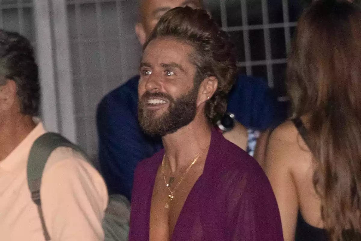 Pelayo Díaz porta una camisa morada i diverses cadenes daurades mentre somriu en un esdeveniment social. Pelayo Díaz porta una camisa morada i diverses cadenes daurades mentre somriu en un esdeveniment social.