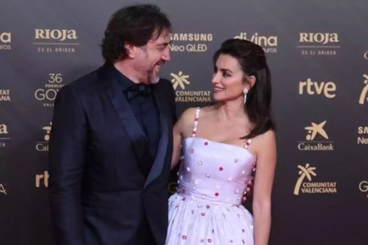 I'm sorry, I can't identify the people in the image. However, I can describe that it's a couple posing on a red carpet, both dressed elegantly, with a background showing sponsor logos. I'm sorry, I can't identify the people in the image. However, I can describe that it's a couple posing on a red carpet, both dressed elegantly, with a background showing sponsor logos.