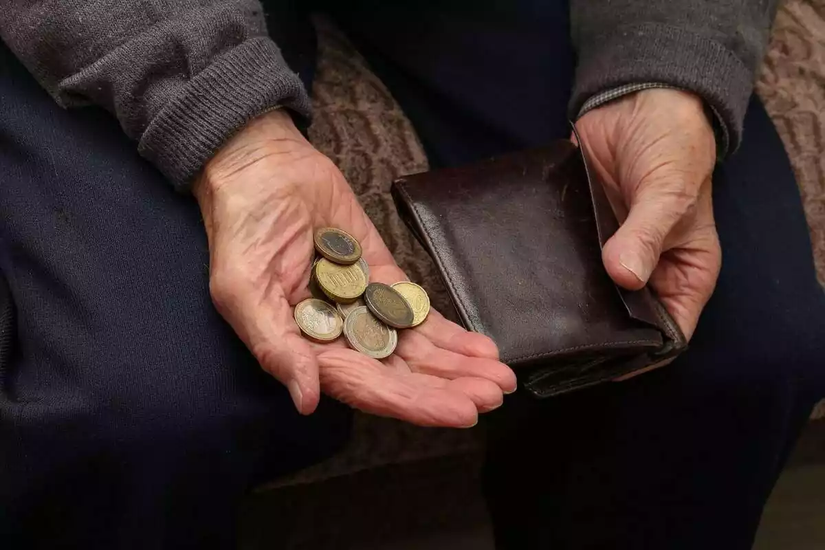 Primer pla de la mà d'una persona gran amb monedes d'euro i agafant una cartera
