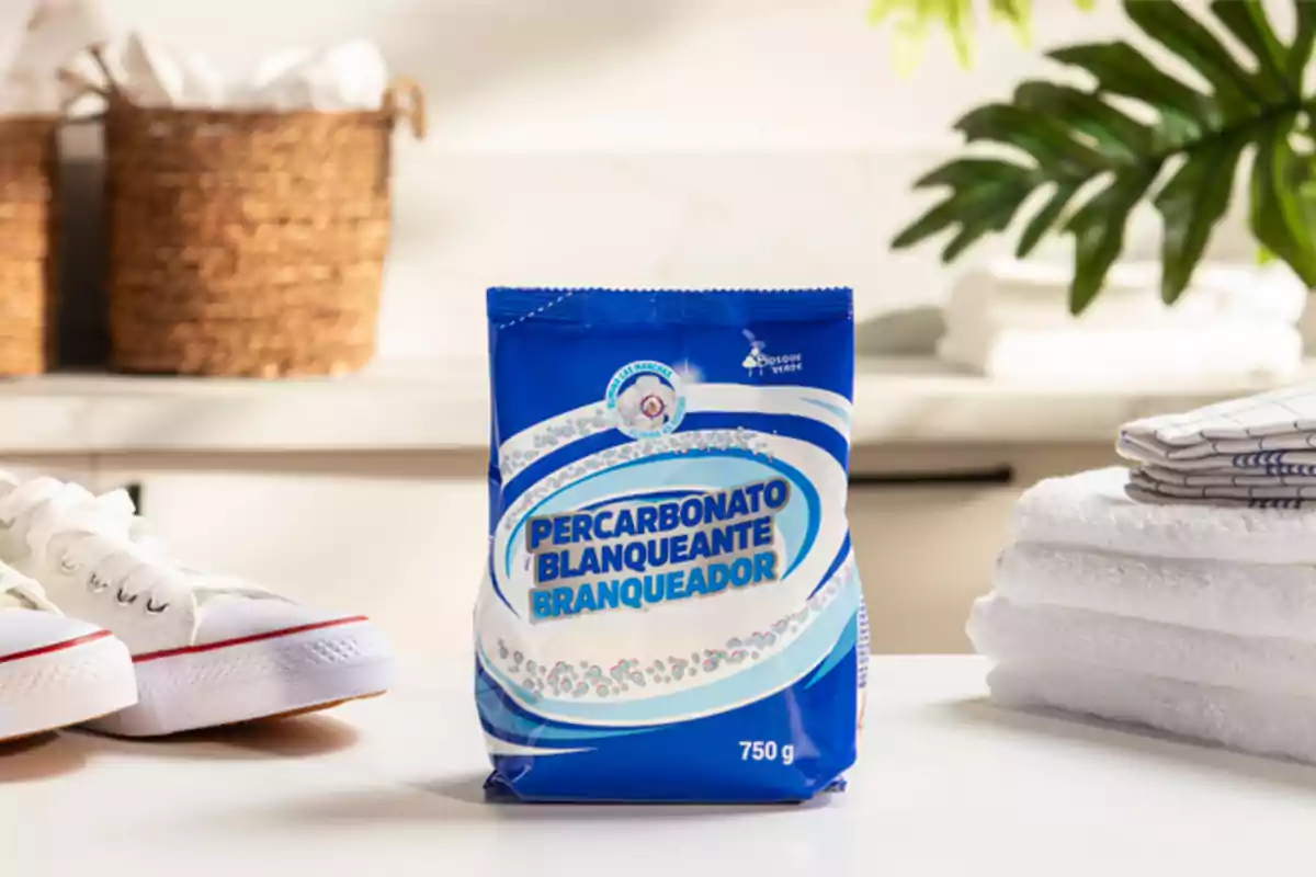 A 750g bag of percarbonate of bleach on a table, with white towels, white shoes and wicker baskets in the background.