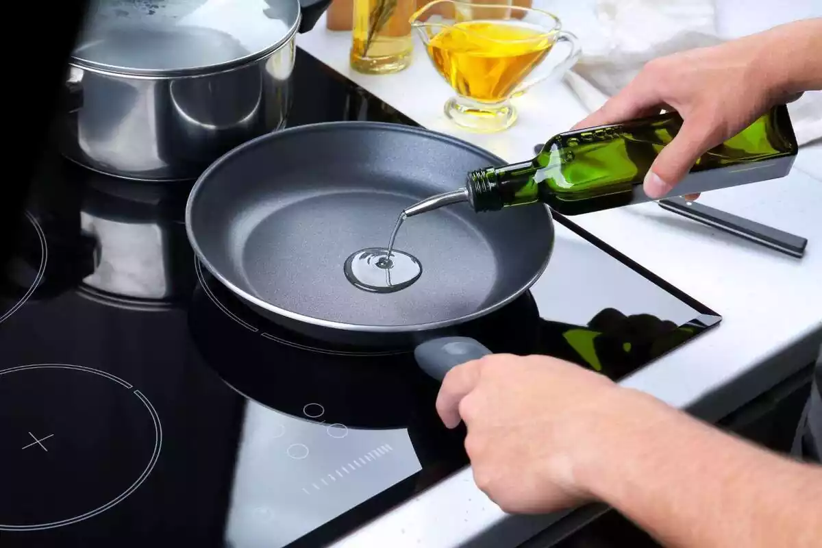 Persona afegint oli a una paella Persona afegint oli a una paella