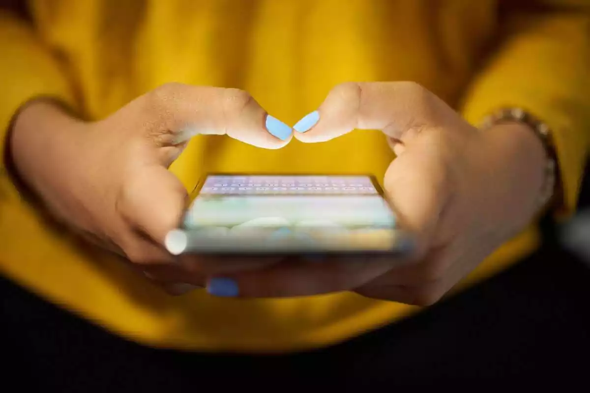 Mans d'una persona amb les ungles pintades de blau, escrivint en un mòbil