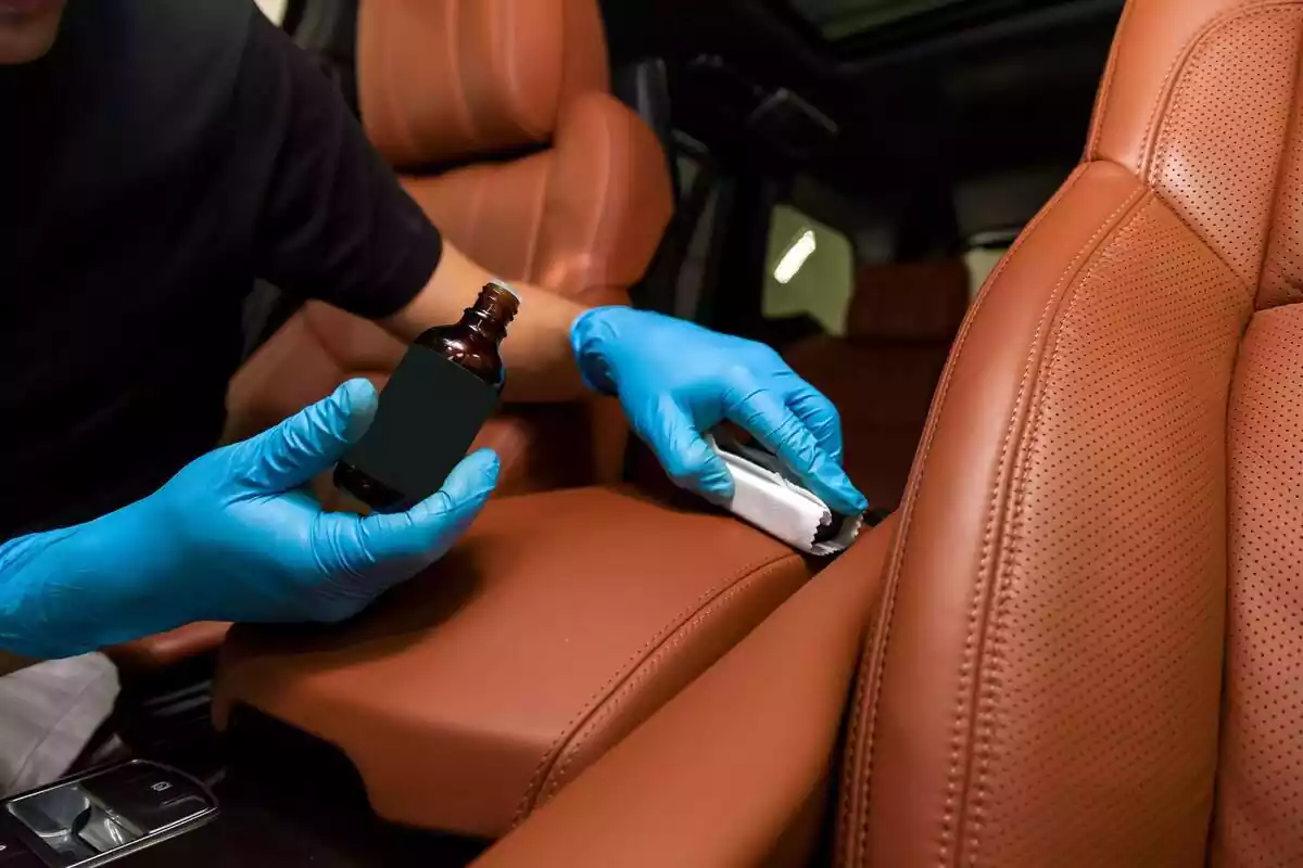 Mans d'una persona amb guants blaus netejant la tapisseria del cotxe