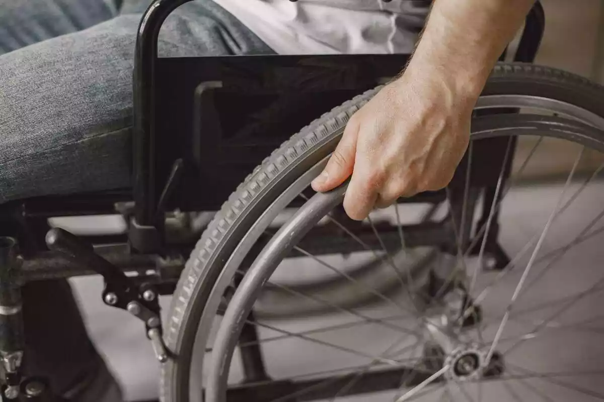 Una persona amb cadira de rodes i la mà tocant una roda