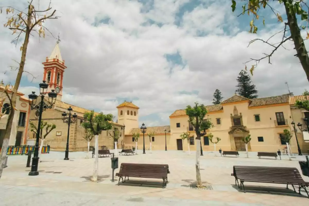 Plaça àmplia amb bancs, arbres podats, fanals negres i edificis històrics de fons sota un cel parcialment ennuvolat Plaça àmplia amb bancs, arbres podats, fanals negres i edificis històrics de fons sota un cel parcialment ennuvolat