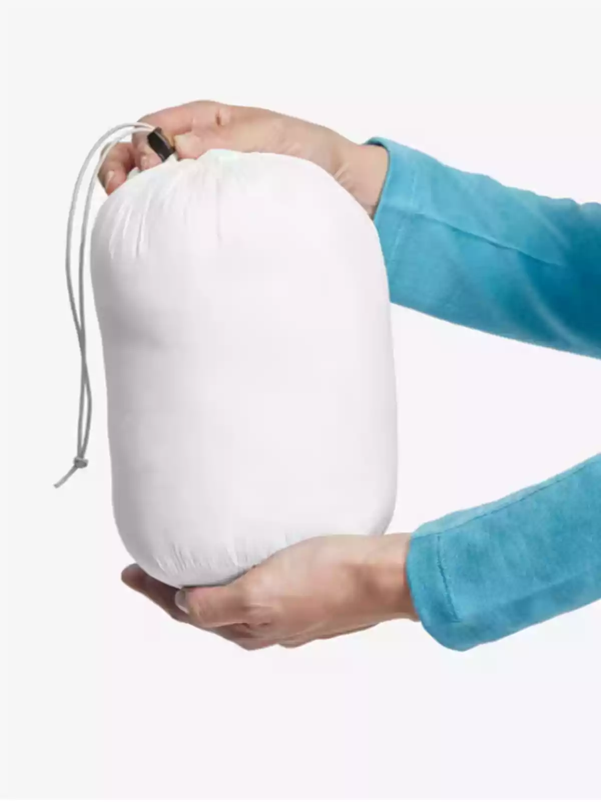 Persona sostenint un sac de dormir compacte de color blanc amb una mà.