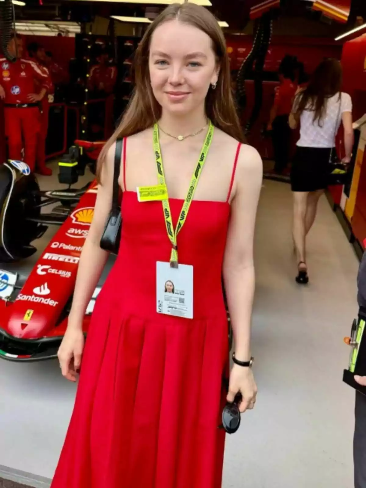 Alejandra de Hannover amb un vestit vermell i una acreditació penjada al coll està dreta davant d'un cotxe de carreres en un garatge. Alejandra de Hannover amb un vestit vermell i una acreditació penjada al coll està dreta davant d'un cotxe de carreres en un garatge.