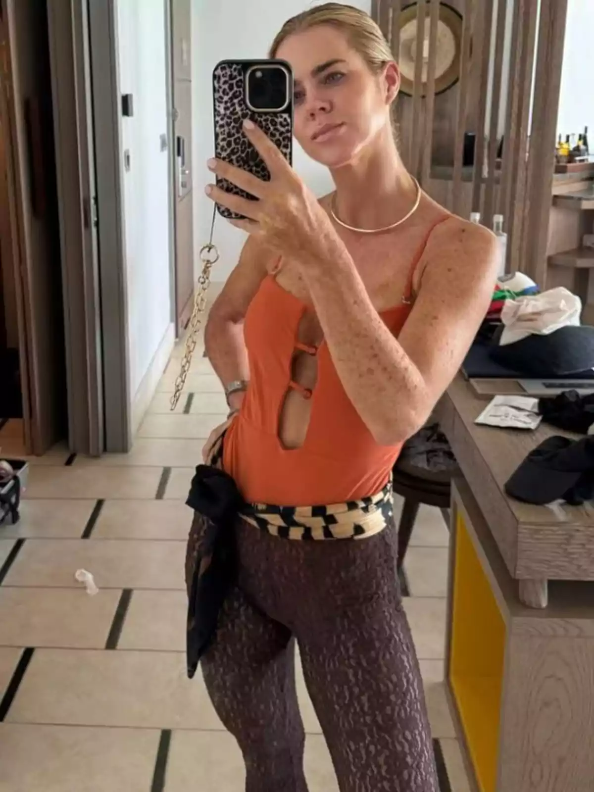 Amelia Bono es fa una selfie davant d'un mirall portant un banyador taronja i malles fosques amb un cinturó estampat, en un ambient interior modern. Amelia Bono es fa una selfie davant d'un mirall portant un banyador taronja i malles fosques amb un cinturó estampat, en un ambient interior modern.