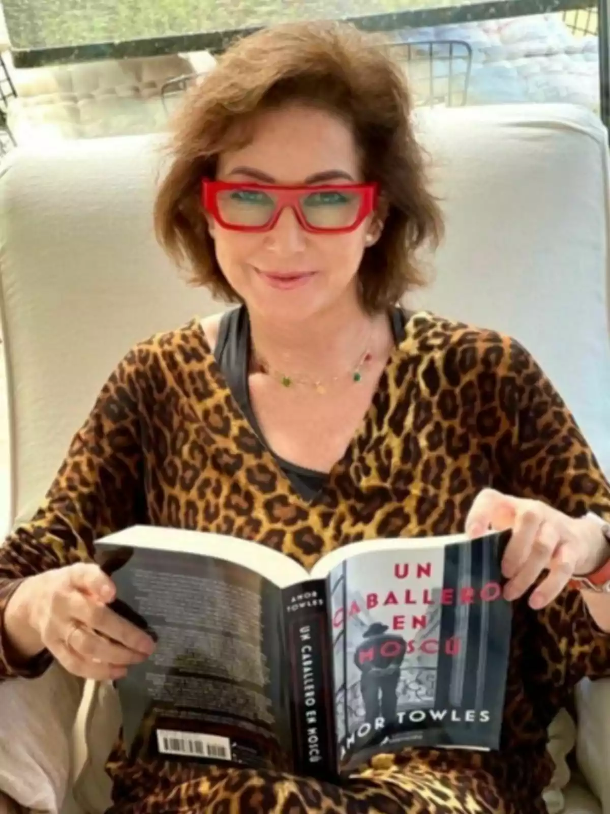 Ana Rosa Quintana amb ulleres vermelles i un vestit d'estampat animal està asseguda llegint un llibre titulat Ana Rosa Quintana amb ulleres vermelles i un vestit d'estampat animal està asseguda llegint un llibre titulat