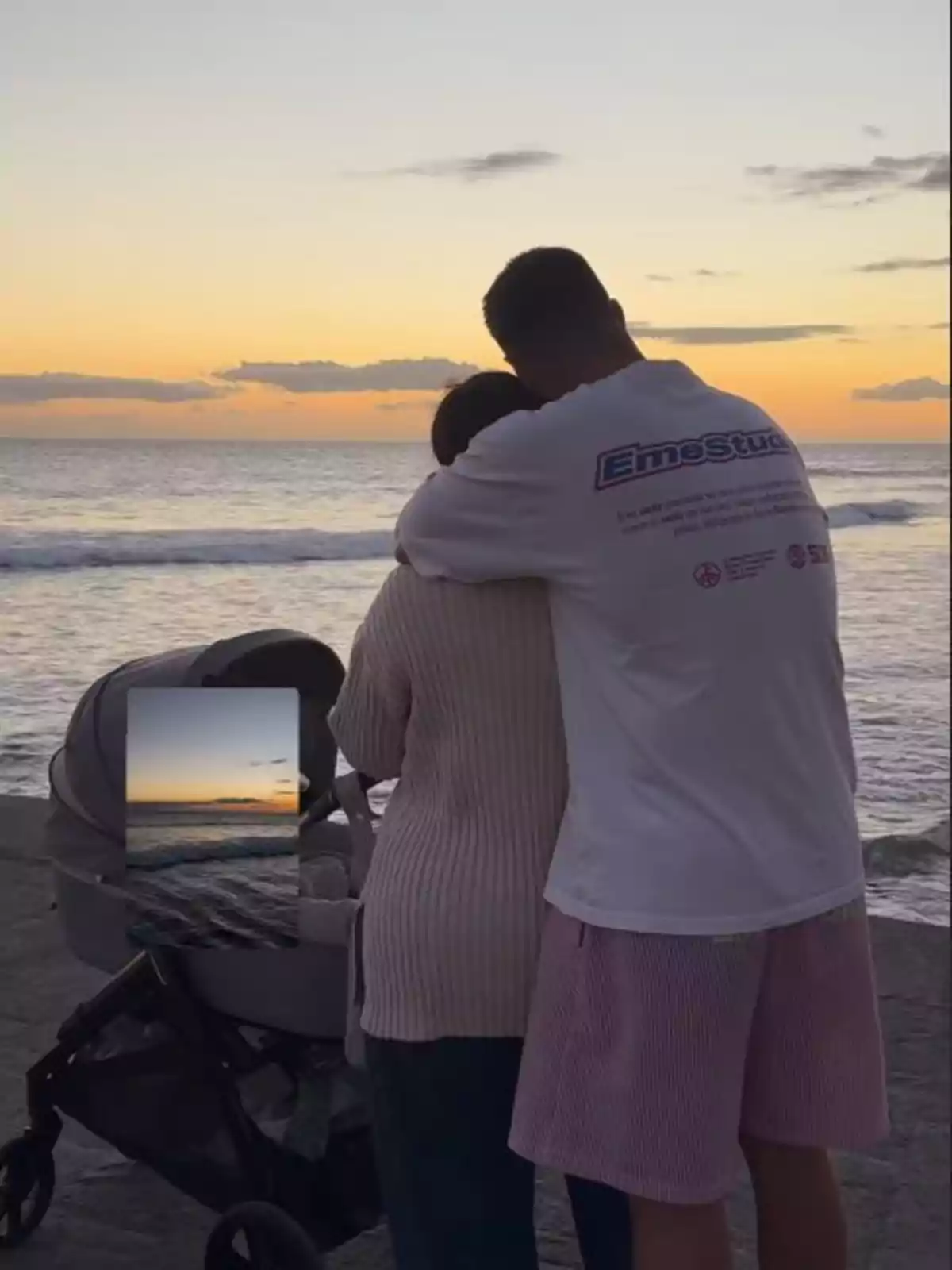 Anabel Pantoja i David Rodríguez s'abracen mentre observen la posta de sol vora el mar amb un cotxet de nadó al seu costat.