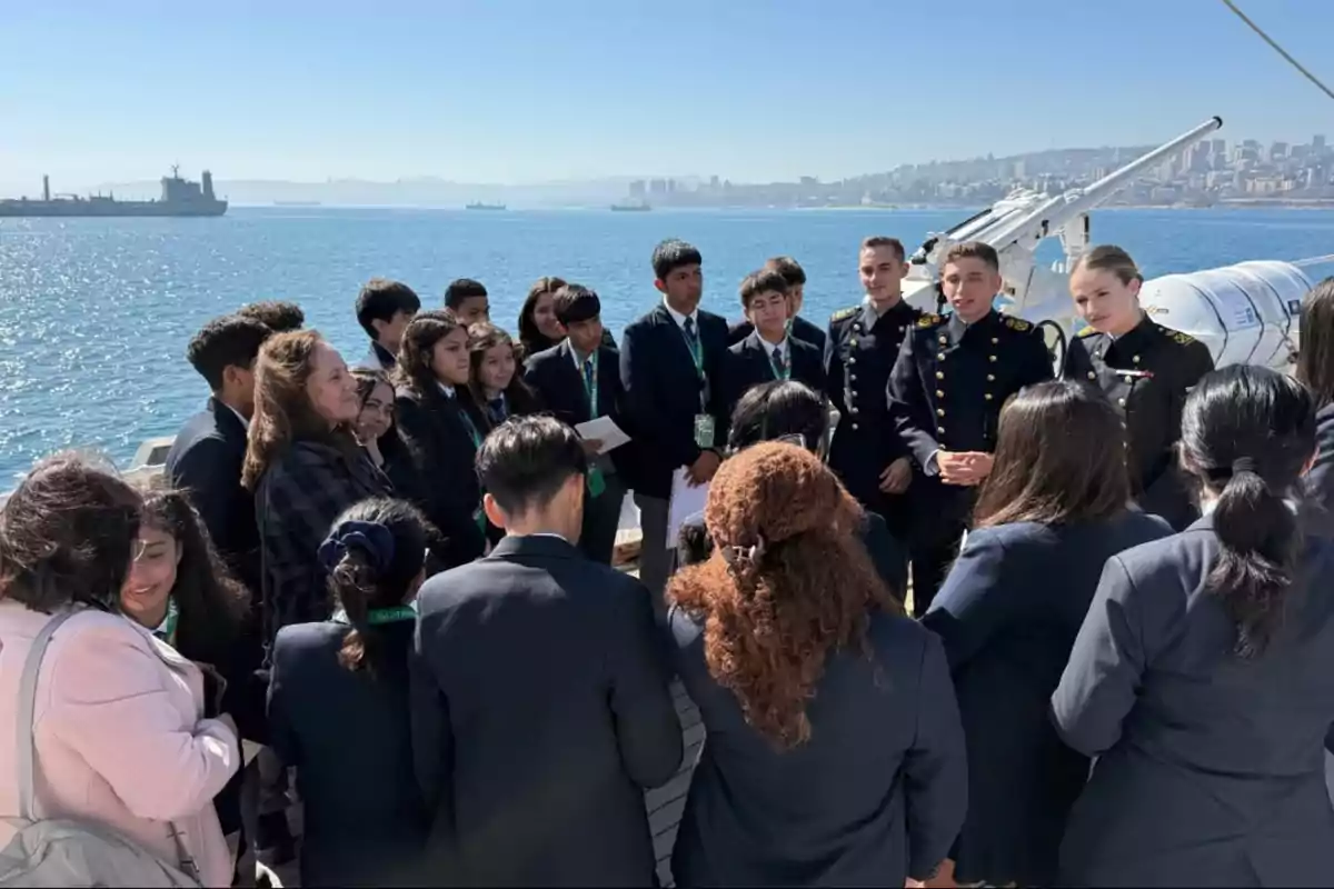 A group of formally dressed people is gathered on the deck of a ship with the sea and a city in the background. A group of formally dressed people is gathered on the deck of a ship with the sea and a city in the background.