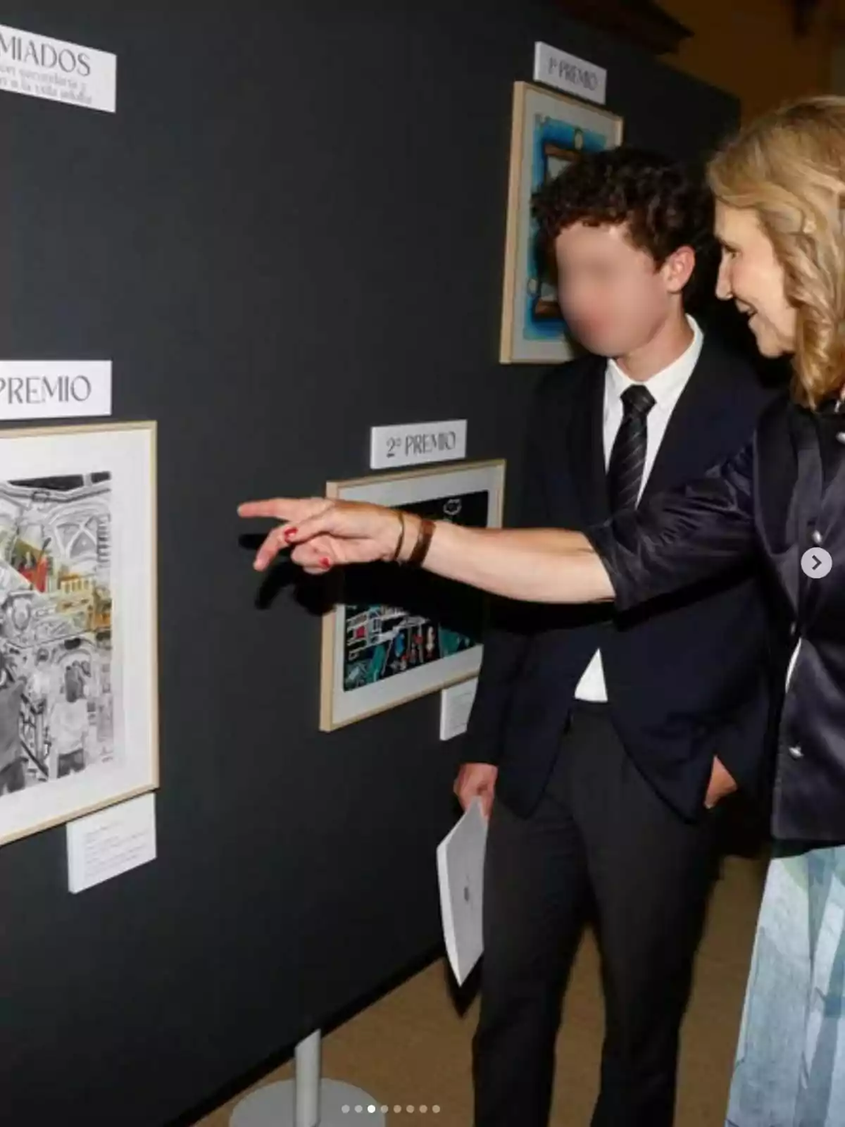 La infanta Elena assenyala una obra d'art en una exposició mentre un jove amb vestit l'observa. La infanta Elena assenyala una obra d'art en una exposició mentre un jove amb vestit l'observa.
