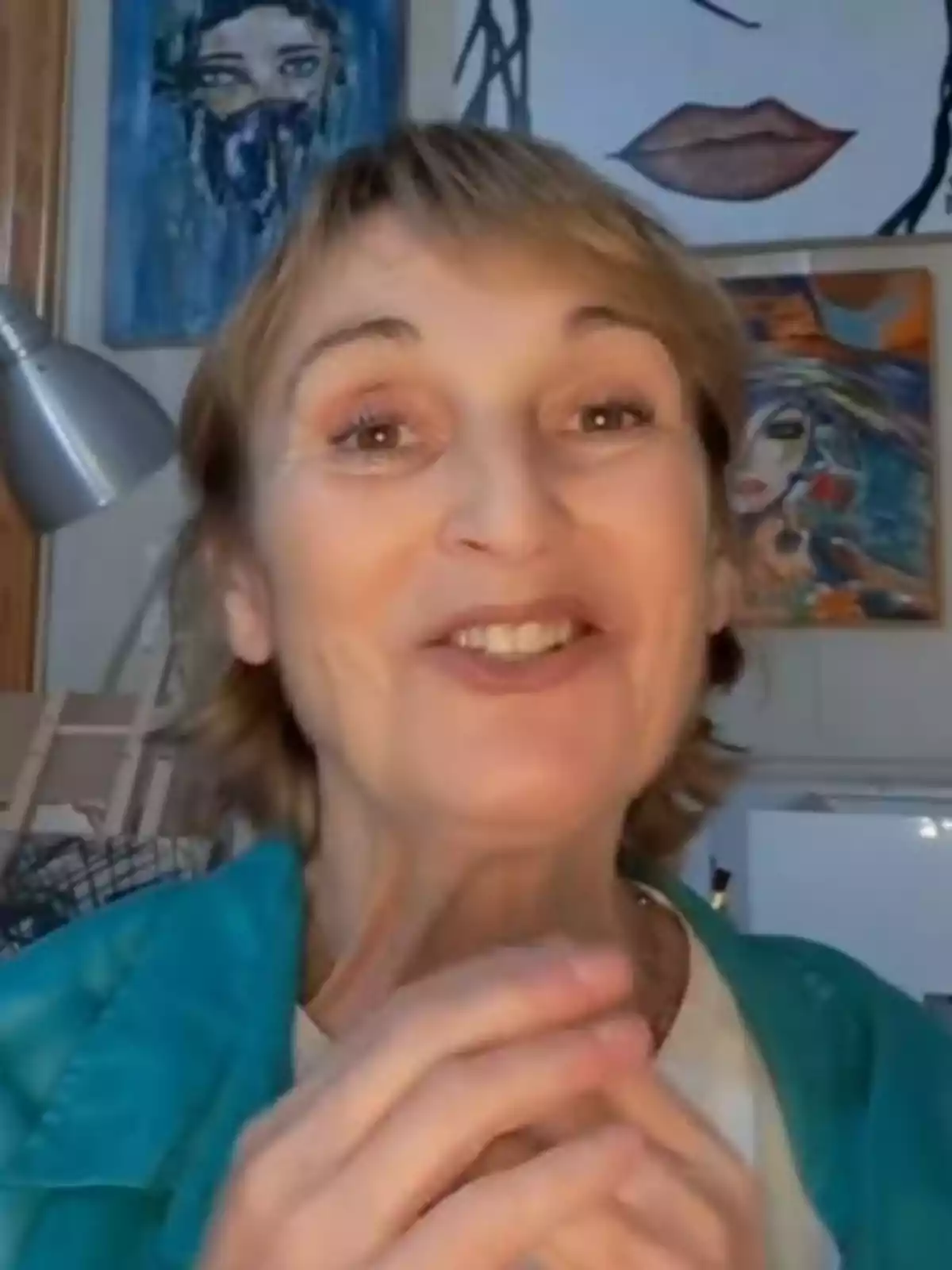 Cristina Fenollar somrient, amb cabell curt i ros, vestida amb una jaqueta blava, en una habitació amb diverses pintures colorides a la paret del fons. Cristina Fenollar somrient, amb cabell curt i ros, vestida amb una jaqueta blava, en una habitació amb diverses pintures colorides a la paret del fons.
