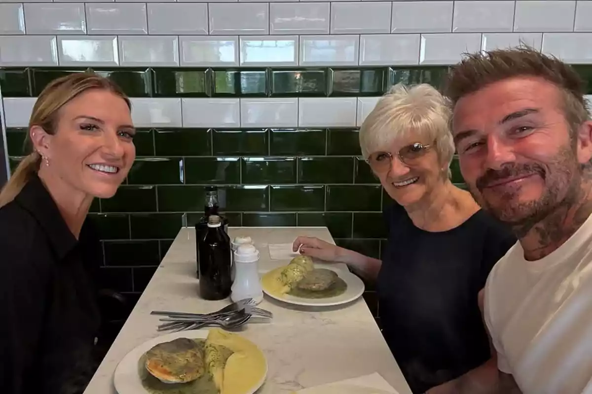 David Beckham, his sister, and his mother are smiling while sitting at a restaurant table with plates of food in front of them and a background of green and white tiled walls. David Beckham, his sister, and his mother are smiling while sitting at a restaurant table with plates of food in front of them and a background of green and white tiled walls.