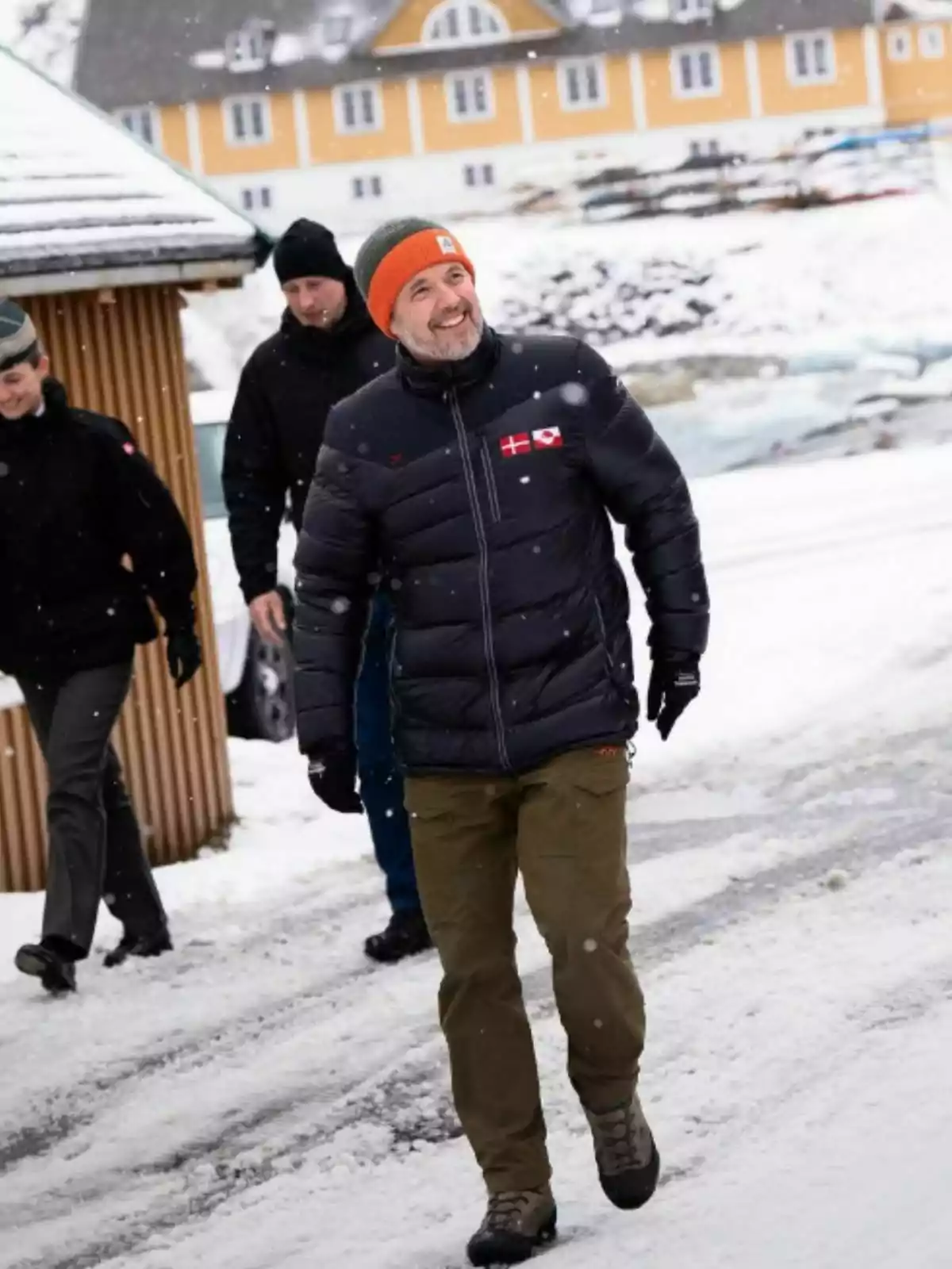Un grup de persones camina per un camí nevat davant d'un edifici groc, mentre cau neu. Un grup de persones camina per un camí nevat davant d'un edifici groc, mentre cau neu.