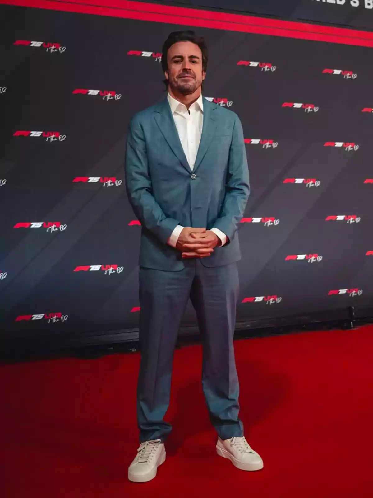 Fernando Alonso con traje azul y zapatillas blancas posando en una alfombra roja frente a un fondo con logotipos. Fernando Alonso con traje azul y zapatillas blancas posando en una alfombra roja frente a un fondo con logotipos.