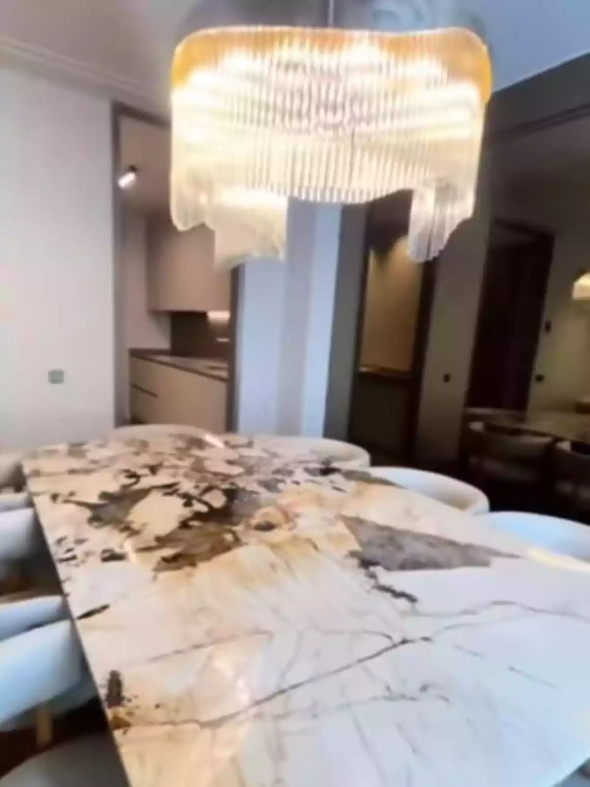Taula de marbre amb vetes fosques envoltada de cadires blanques sota una làmpada penjant de disseny modern en un menjador elegant Taula de marbre amb vetes fosques envoltada de cadires blanques sota una làmpada penjant de disseny modern en un menjador elegant