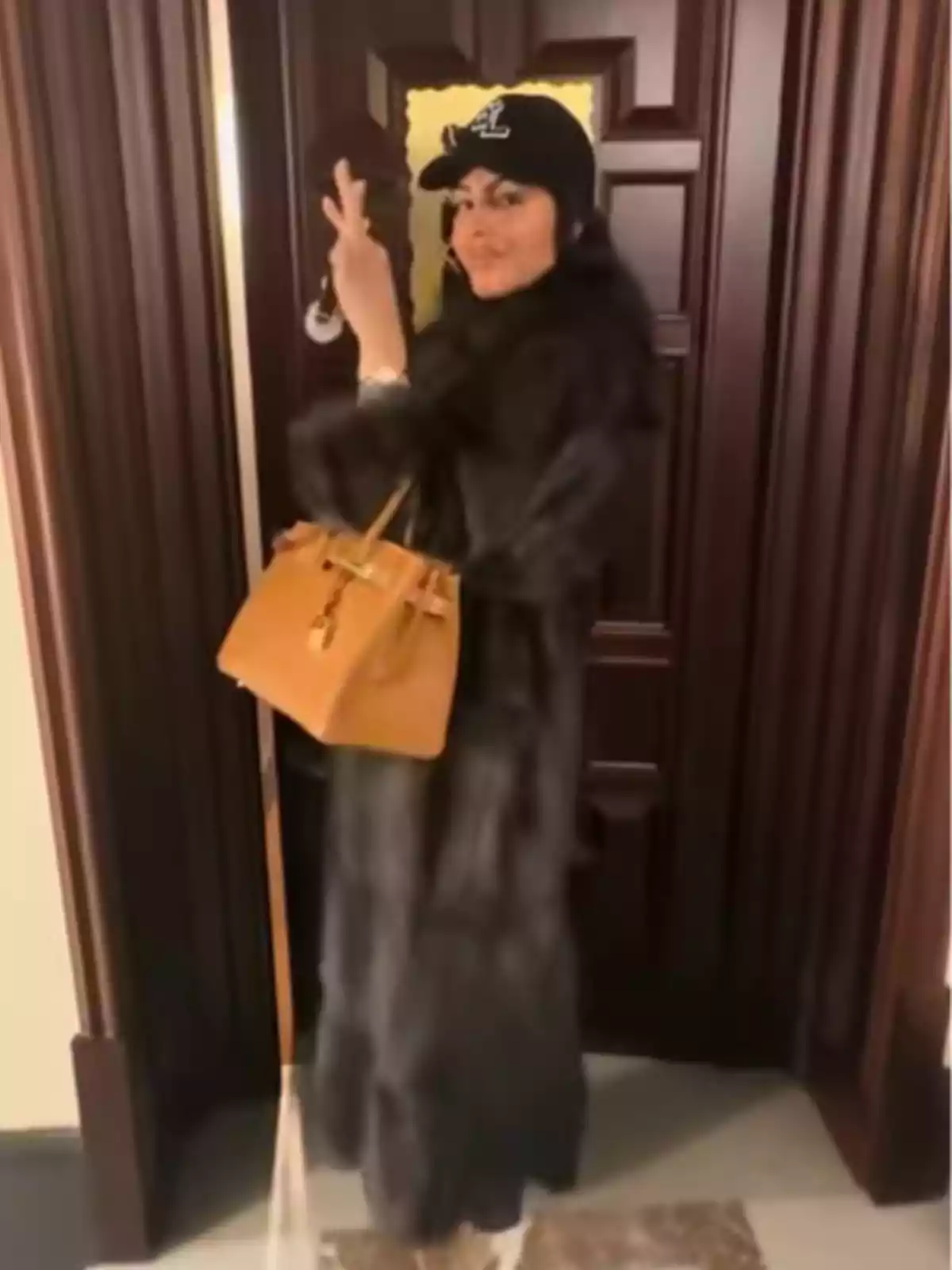 Georgina Rodríguez amb abric fosc i gorra negra posant davant d’una porta de fusta mentre sosté una bossa marró i fa el signe de pau amb la mà Georgina Rodríguez amb abric fosc i gorra negra posant davant d’una porta de fusta mentre sosté una bossa marró i fa el signe de pau amb la mà