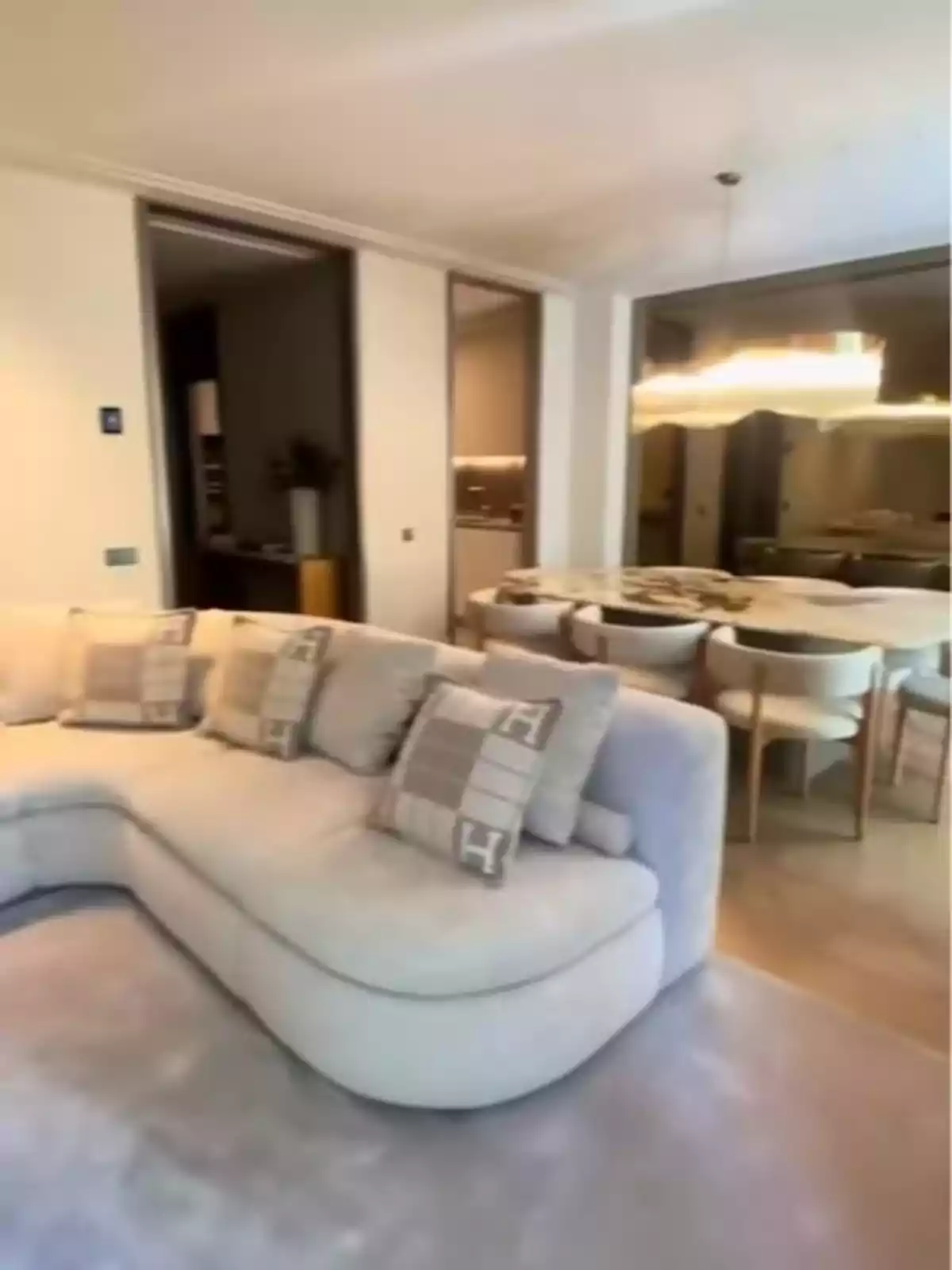 Sala moderna amb sofà en forma de L de color clar, coixins decoratius, taula de menjador amb diverses cadires i làmpada penjant. Sala moderna amb sofà en forma de L de color clar, coixins decoratius, taula de menjador amb diverses cadires i làmpada penjant.