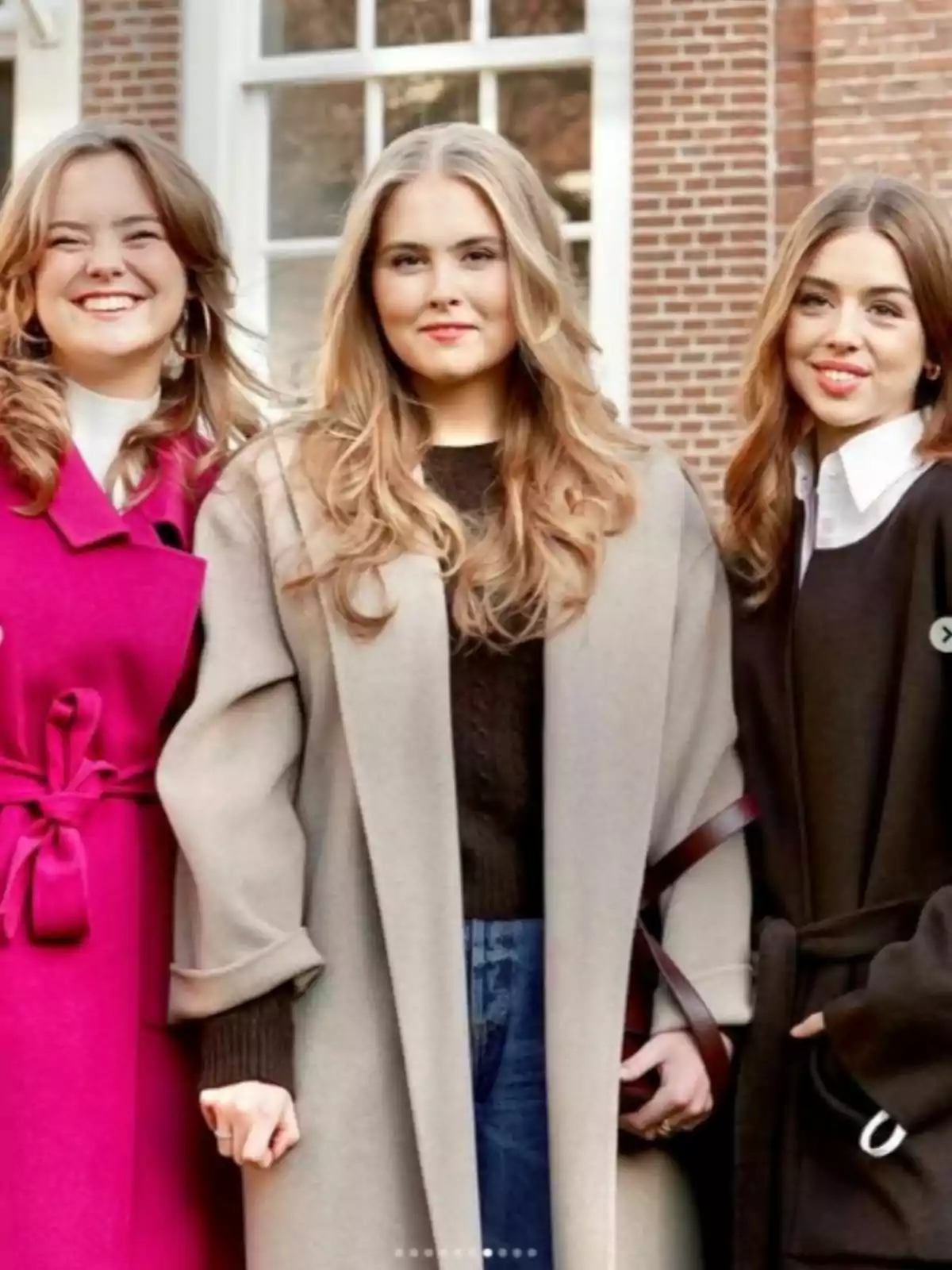 Ariane, Amalia, and Alexia of the Netherlands pose together outdoors, wearing elegant coats and smiling in front of a brick building with large windows. Ariane, Amalia, and Alexia of the Netherlands pose together outdoors, wearing elegant coats and smiling in front of a brick building with large windows.