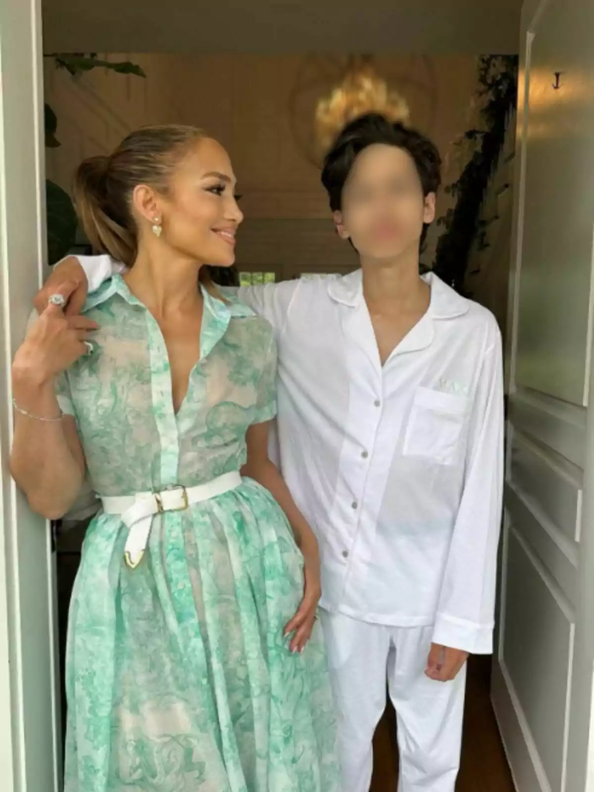 Jennifer Lopez con un vestido verde claro estampado y Max con pijama blanca posan juntas en una entrada. Jennifer Lopez con un vestido verde claro estampado y Max con pijama blanca posan juntas en una entrada.