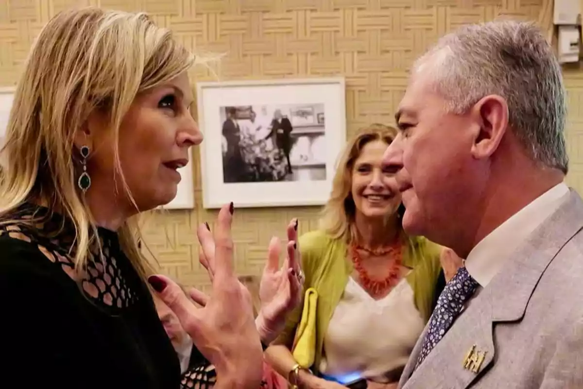 Máxima of the Netherlands and José Luis Sanz chatting animatedly at a social event, with a third person smiling in the background. Máxima of the Netherlands and José Luis Sanz chatting animatedly at a social event, with a third person smiling in the background.