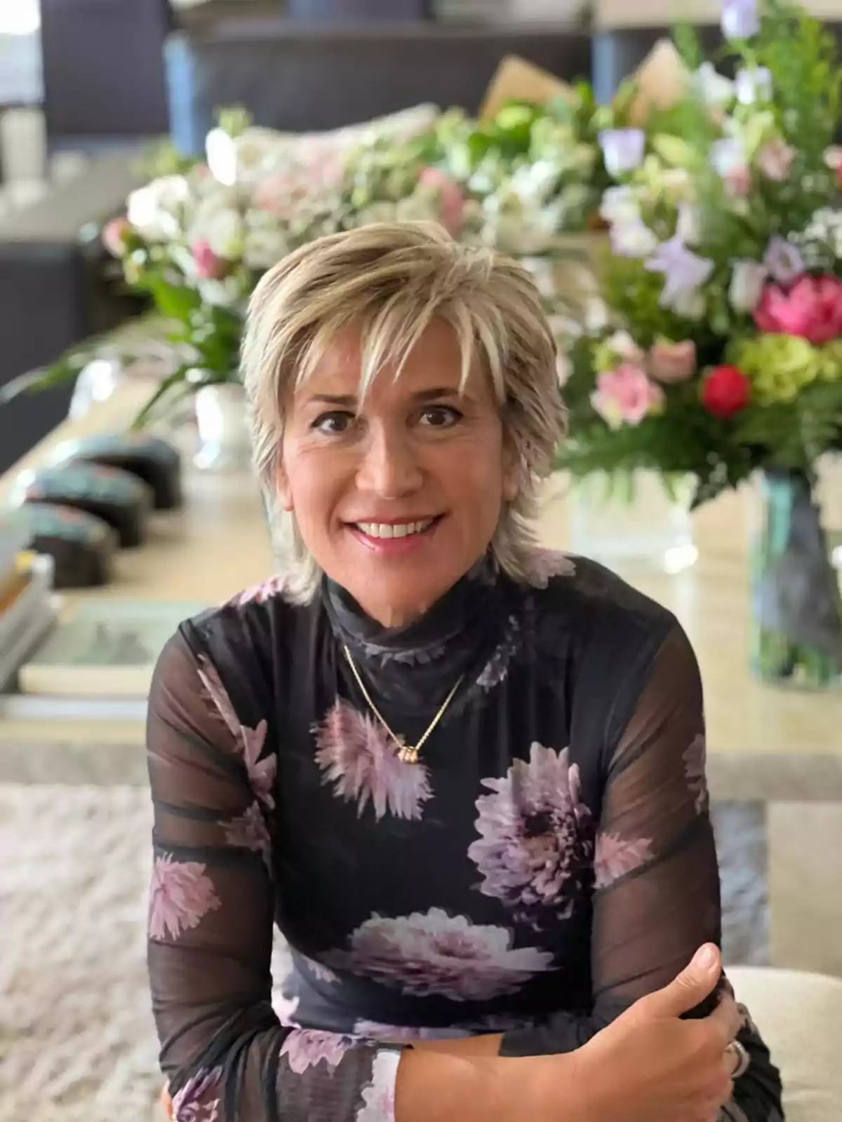 Julia Otero sonriendo con un vestido de flores y un fondo de arreglos florales. Julia Otero sonriendo con un vestido de flores y un fondo de arreglos florales.