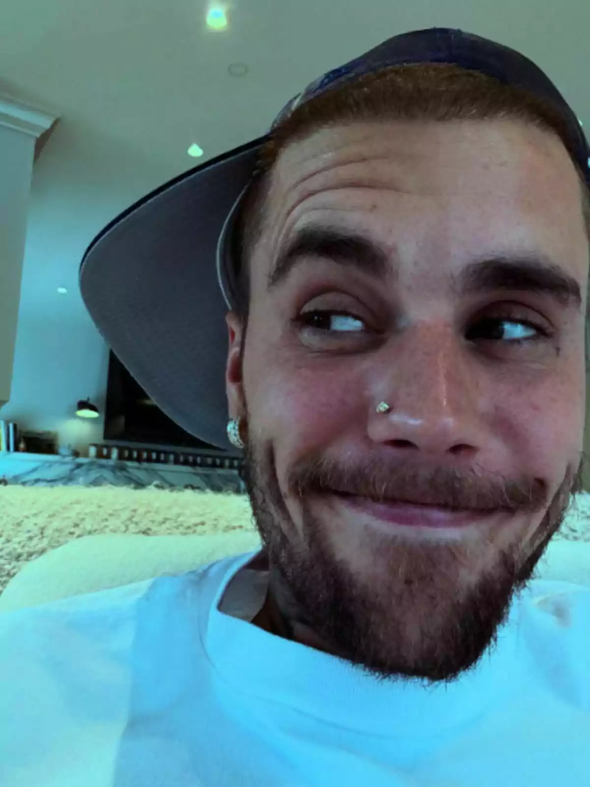Justin Bieber wearing a sideways cap, smiling while looking to the side in a brightly lit room Justin Bieber wearing a sideways cap, smiling while looking to the side in a brightly lit room