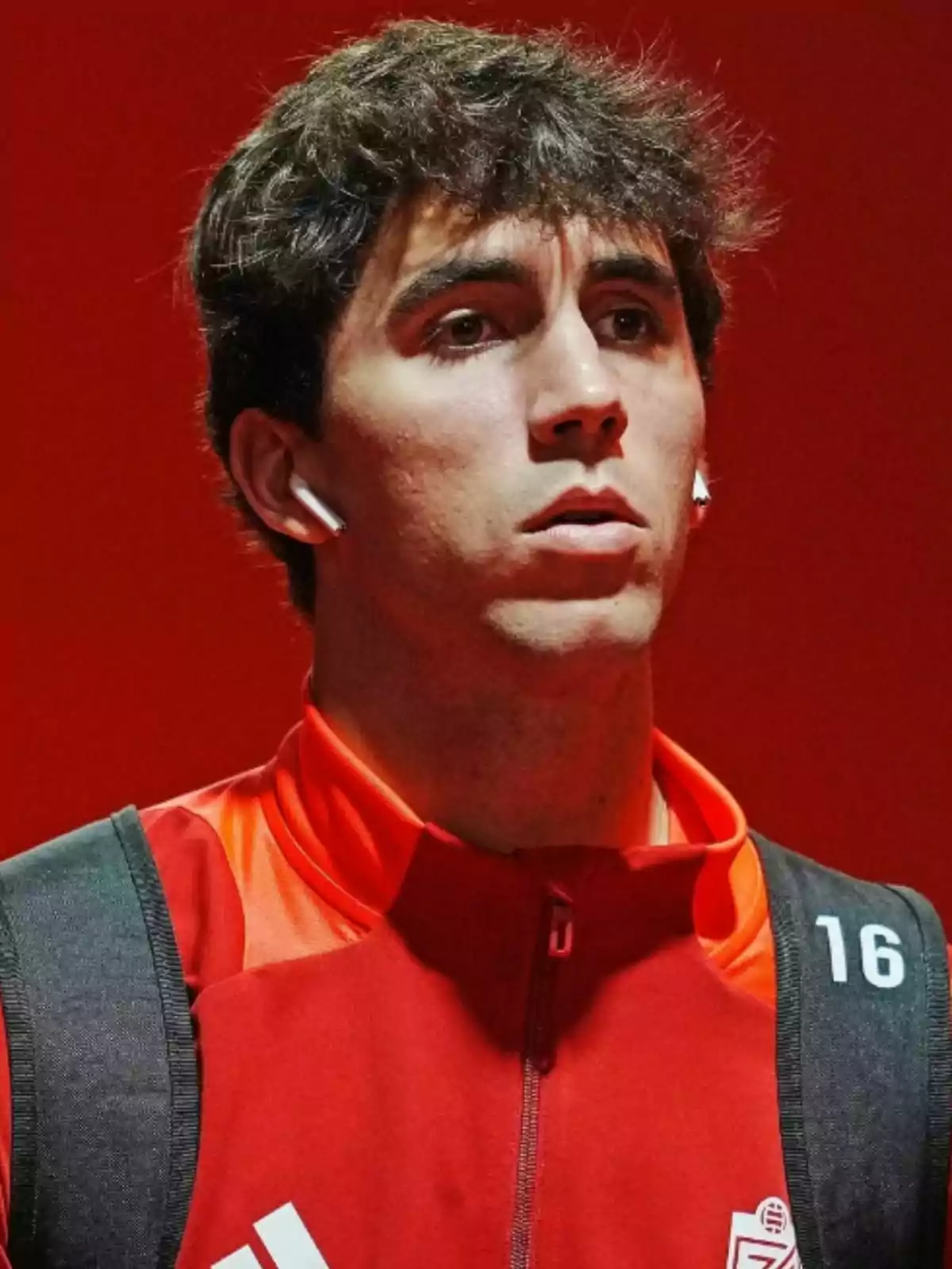 Manu Lama amb auriculars i jaqueta vermella amb el número 16 en un fons vermell. Manu Lama amb auriculars i jaqueta vermella amb el número 16 en un fons vermell.