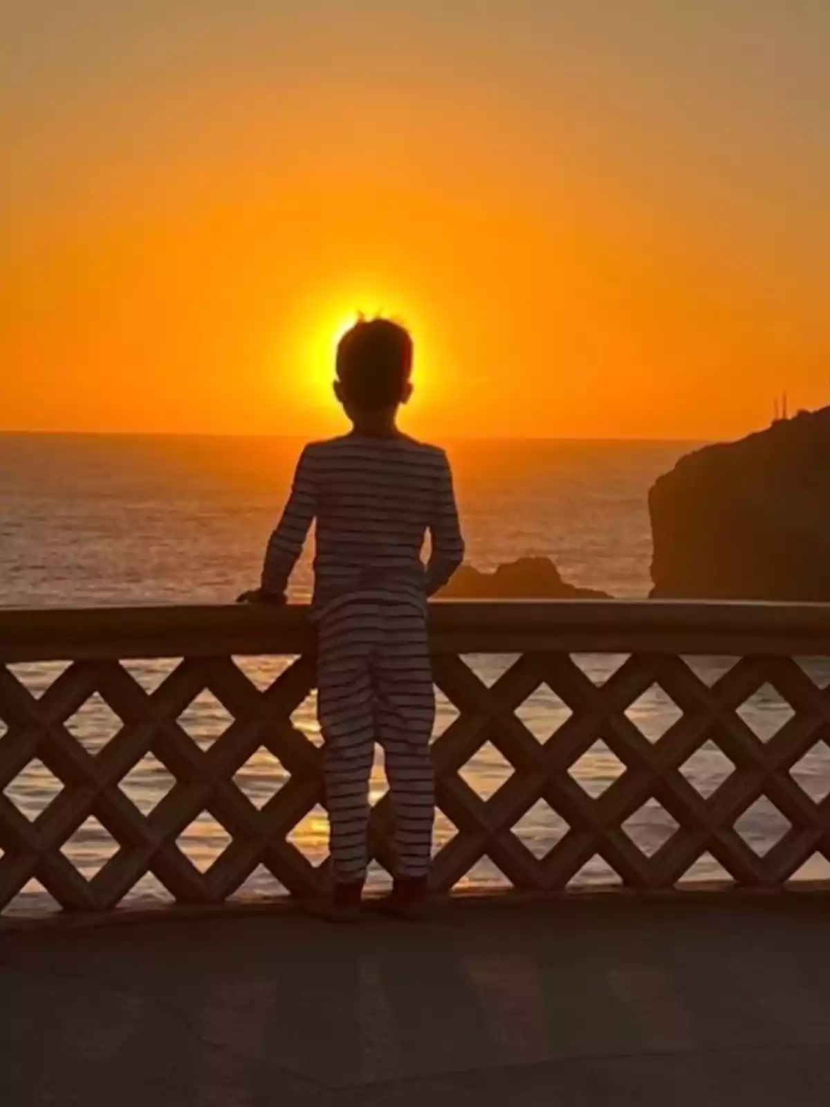 Archie en pijama de ratlles observa la posta de sol des d'un balcó davant del mar. Archie en pijama de ratlles observa la posta de sol des d'un balcó davant del mar.